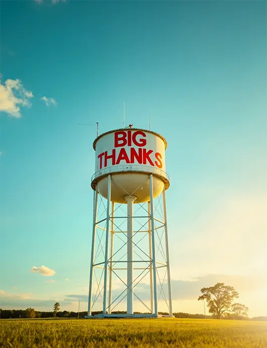 Big Thanks Marketing - Elevating Small Businesses A tall water tower with 'Big Thanks' painted in bold red letters, standing against a clear blue sky at sunset, symbolizing strong marketing and business growth